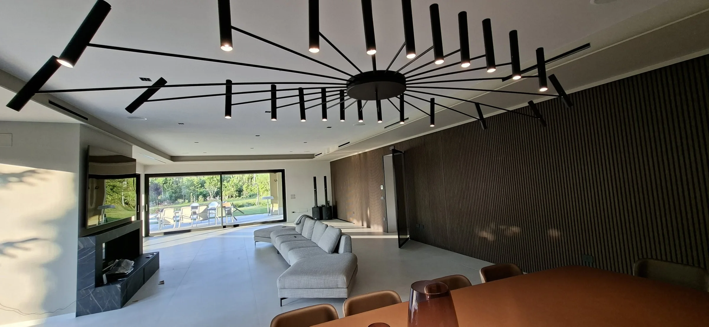 Zona giorno di una villa con parete in legno cannettato, divano su misura e grande vetrata sul giardino